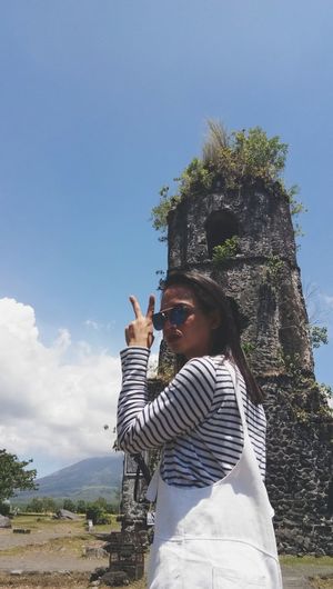 Portrait of young woman showing peace sign against old ruin