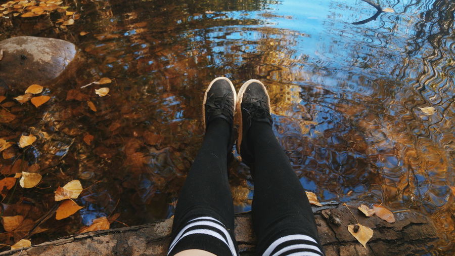 Low section of woman sitting at lakeshore during autumn