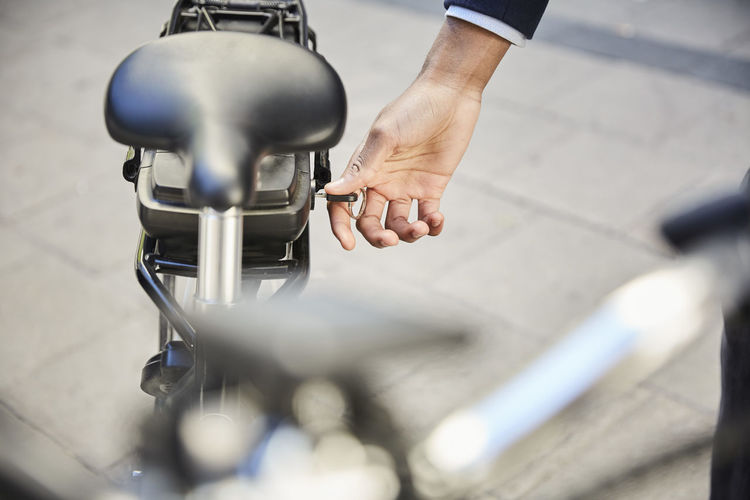 Cropped hand of male commuter locking electric bicycle in city