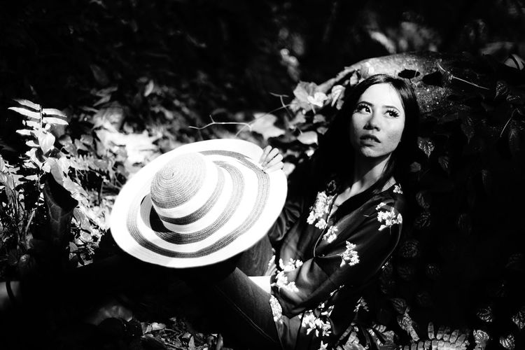Young woman holding sunhat in forest during sunny day