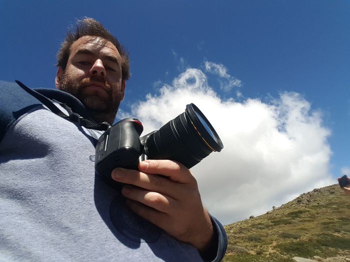 Low angle view of man holding camera against sky