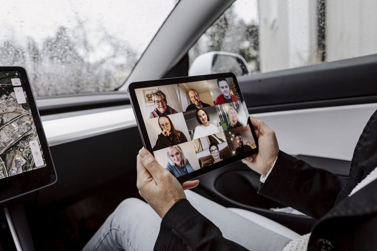 Woman in car holding digital tablet with video conference