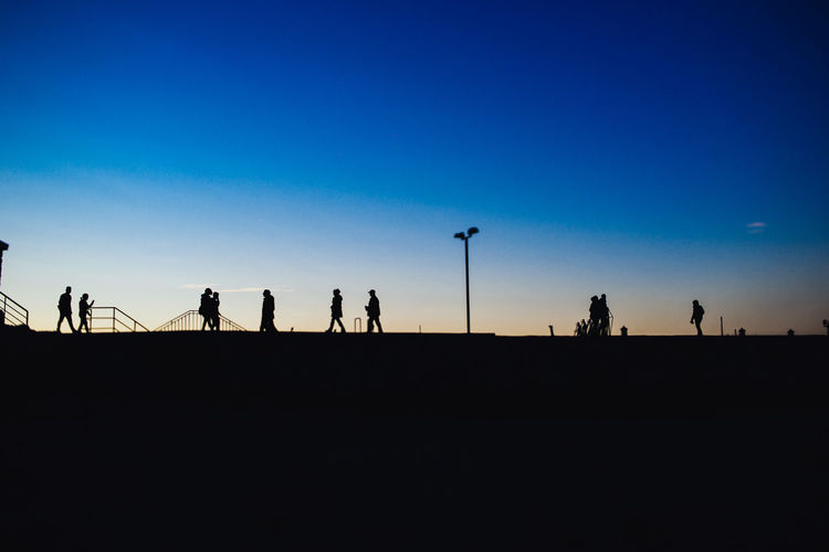 Silhouette people against clear blue sky during sunset