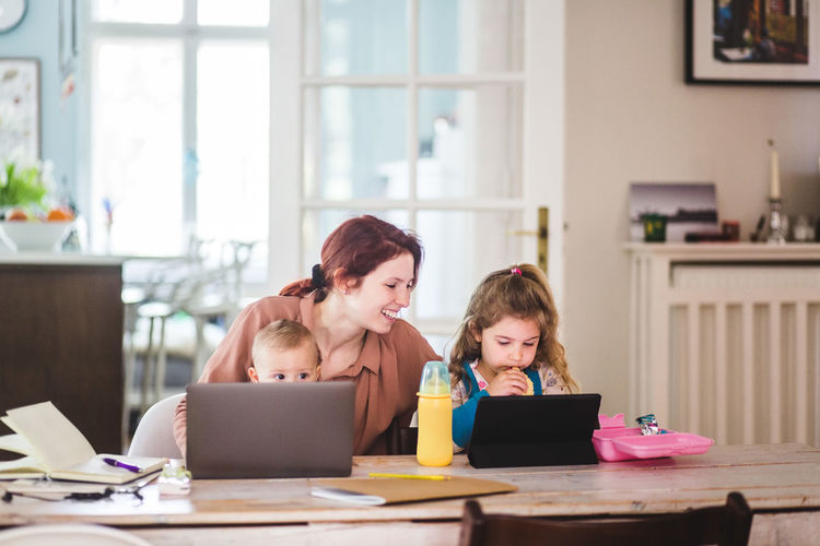 Smiling woman looking at girls watching movie on digital tablet while having food