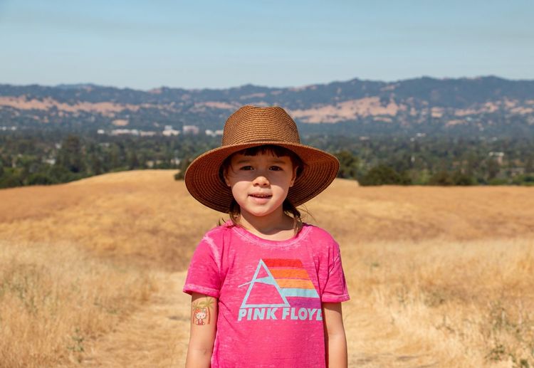 Portrait of cute smiling girl wearing hat standing on field during summer