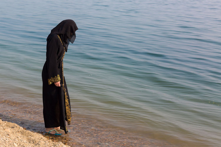 A muslim woman national clothes wets her feet in the sea.