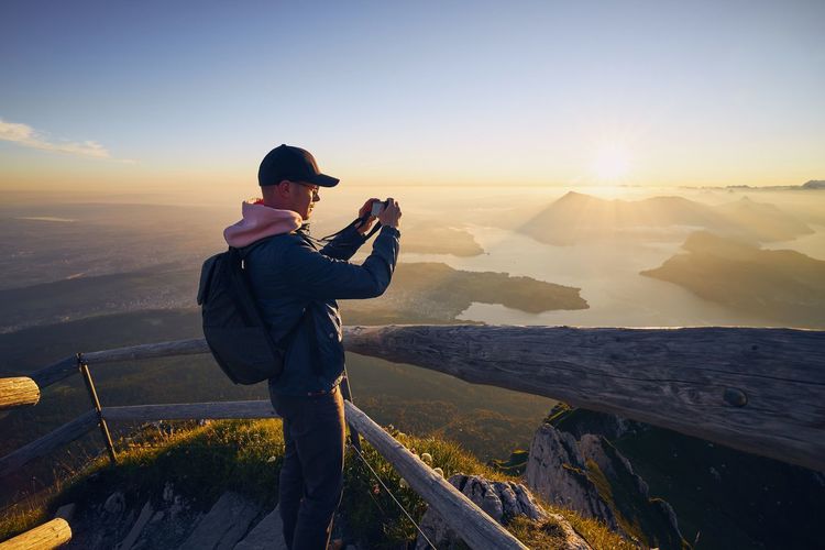 Side view of man photographing while standing against landscape