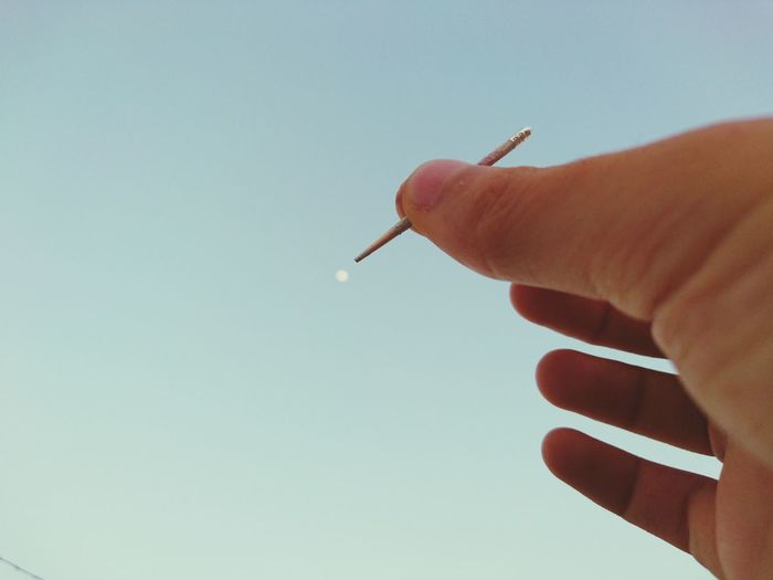 Close-up of hand holding toothpick against sky