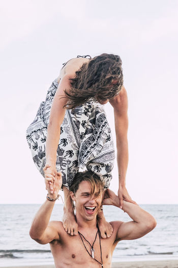 Shirtless young man carrying girlfriend on shoulder at beach