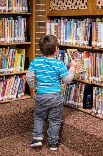 Rear view of boy looking at book in library