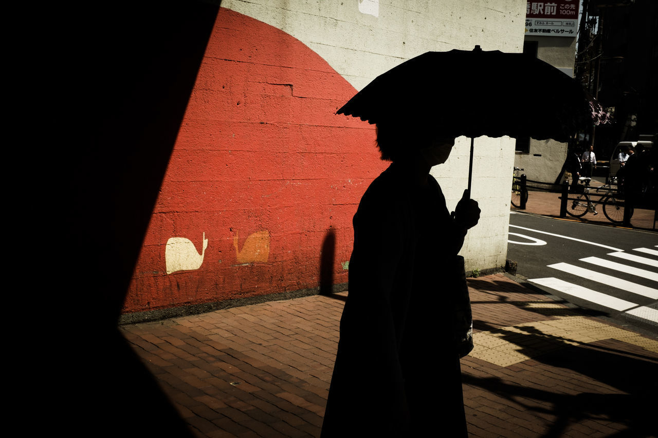 SILHOUETTE WOMAN WALKING ON FOOTPATH IN RAIN
