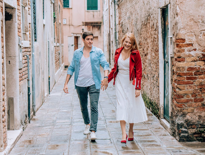Full length of young couple holding hands while walking in alley
