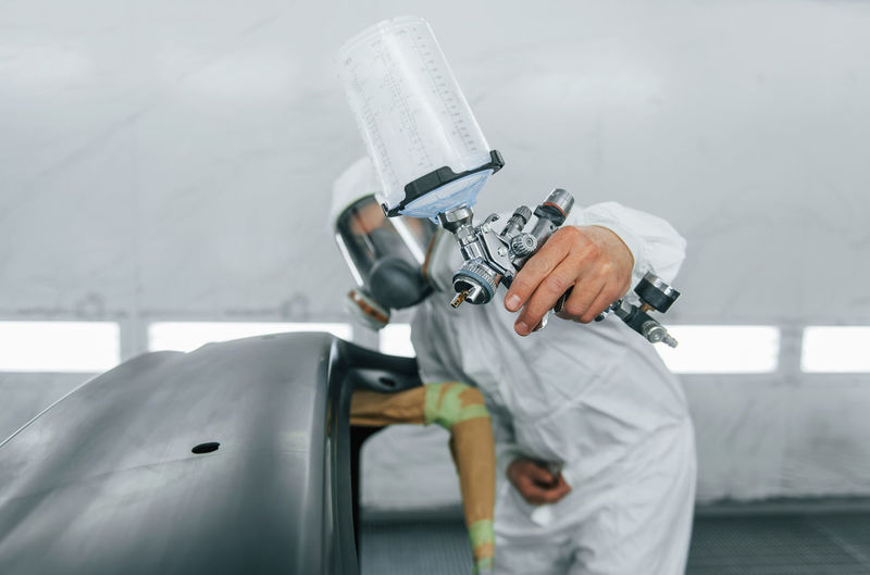 Painting the car. man in uniform is working in the auto service.