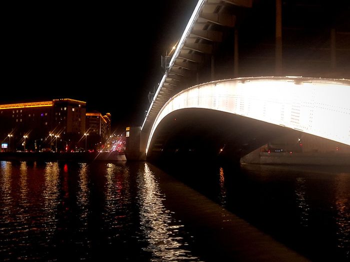 Illuminated bridge over river in city at night