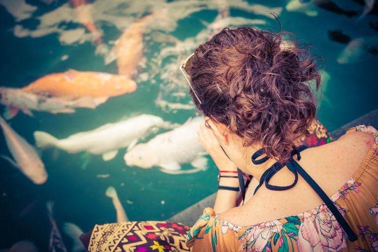 Rear view of woman sitting by pond