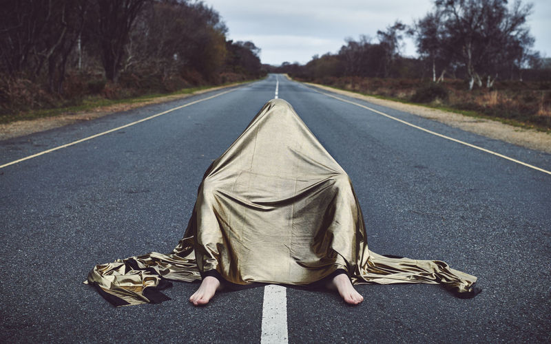 Man covered with fabric sitting on road