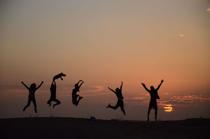 Silhouette people jumping against sky during sunset
