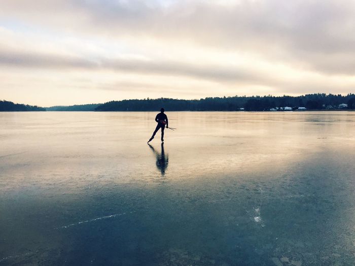 Rear view of person skating on frozen lake against sky