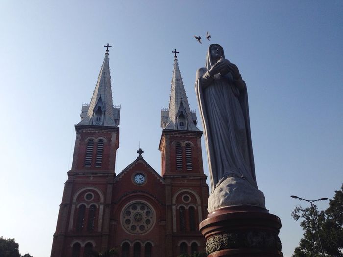 Low angle view of virgin mary statue by church against clear sky