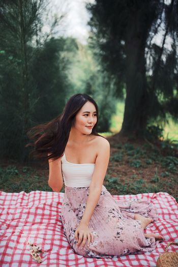 Portrait of beautiful young woman sitting on picnic blanket against trees in forest