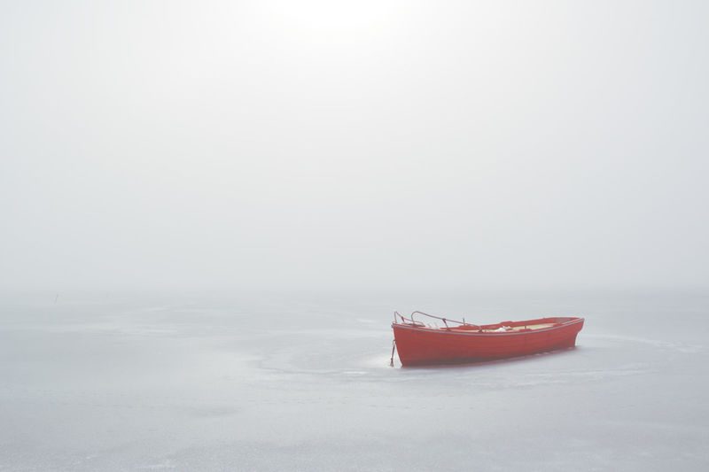 Red boat trapped in frozen lake in misty morning