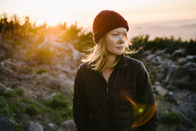 Woman looking away while standing on mountain against sky during sunset