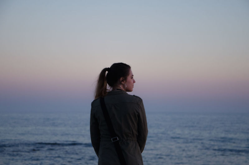 Rear view of woman standing by sea against sky during sunset