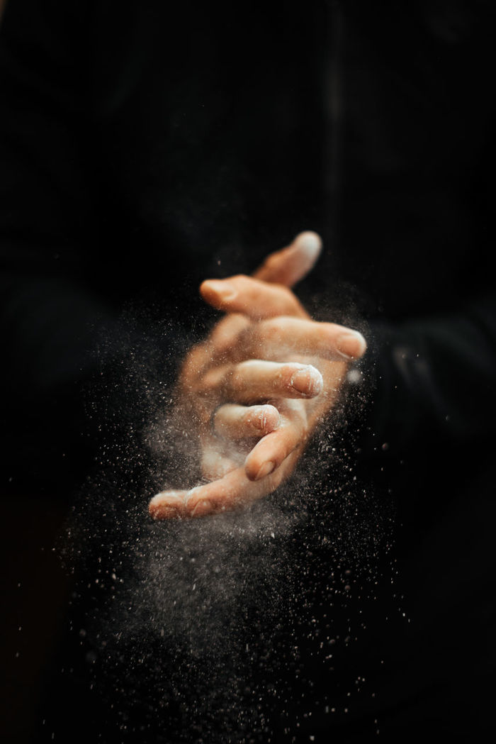 Cropped hands of man dusting sports chalk against black background