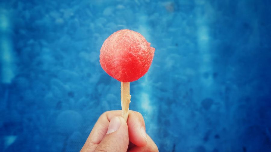 Cropped image of person holding watermelon lollipop