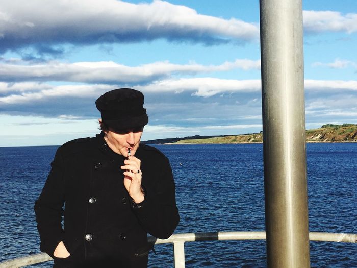 Man smoking by sea against sky