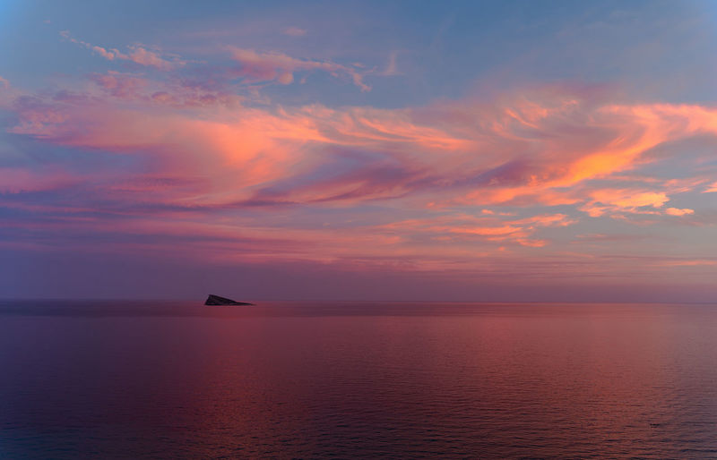 Sunset in benidorm / valencia / spain with a cloudy blue and orange sky and an island at the horizon of the mediterranean sea with a orange, red , blue and pink color. horizontal photo