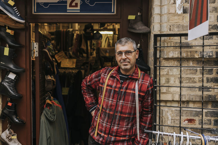 Portrait of mature owner standing with hand on hip outside clothing store