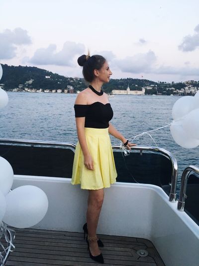 Beautiful woman standing with balloons on yacht in sea against sky