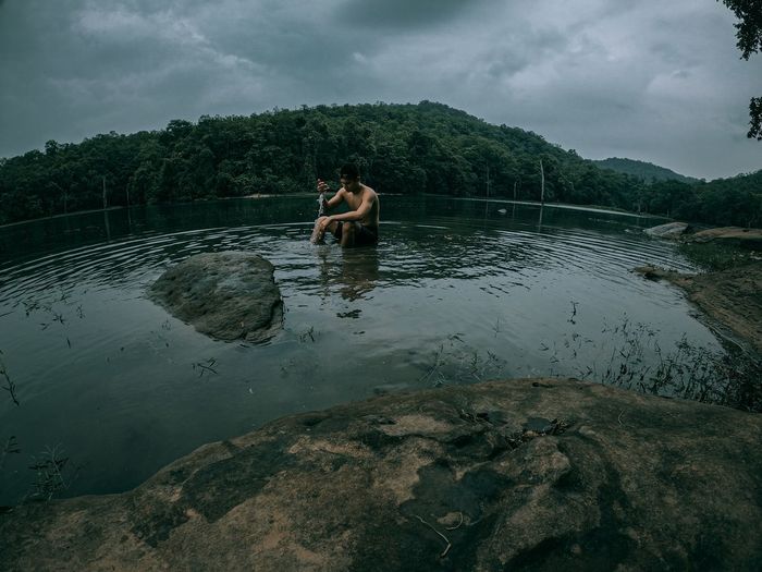 Full length of shirtless man in lake against sky