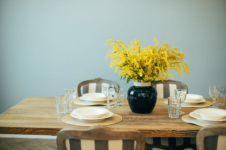 Festive easter table setting. branches of mimosa in vase. home interior.