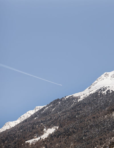 Low angle view of vapor trail over mountain against clear blue sky