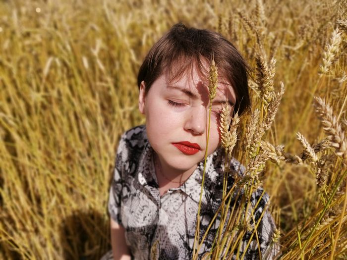Portrait of a young woman with her eyes closed, sitting in a field of wheat. 
