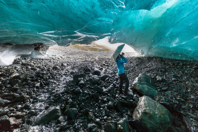 Side view of explorer photographing melting glacier cave