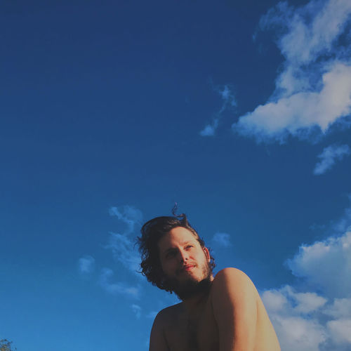 Low angle of young man looking away against blue sky
