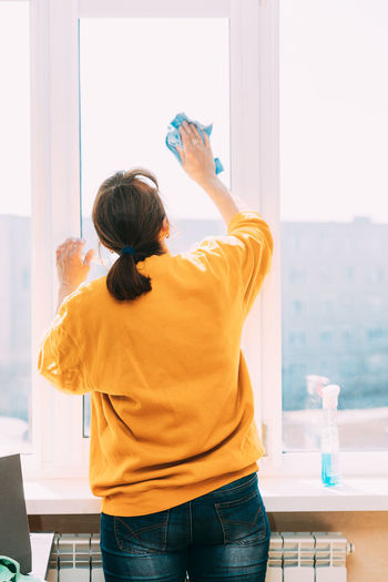 Rear view of woman cleaning window at home