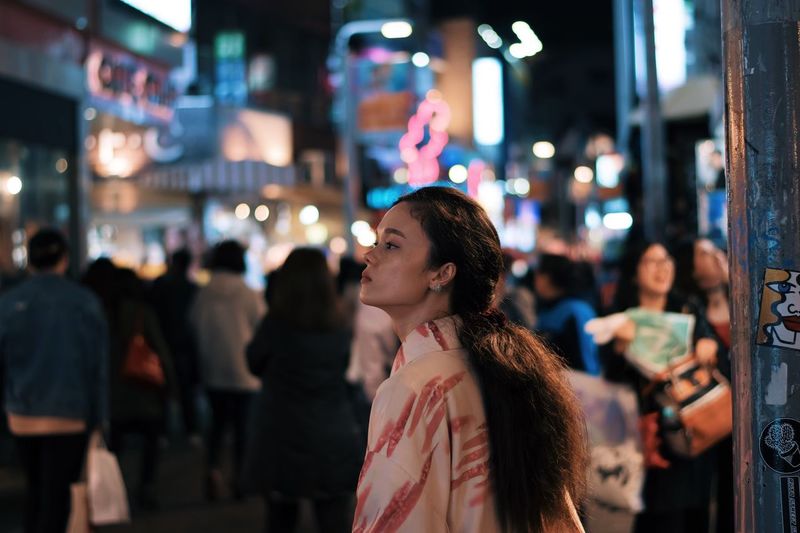 Thoughtful woman standing in illuminated city at night