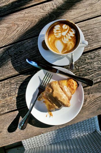 Directly above shot of latte and caramel croissant served on table