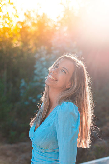 Portrait of smiling young woman standing in forest at sunset