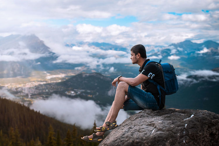 Young man sitting on rock against mountains