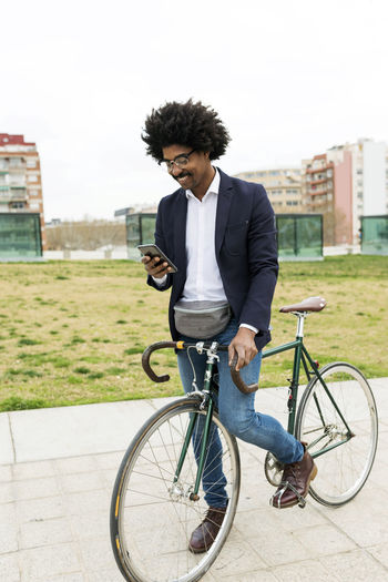 Spain, barcelona, smiling businessman on bicycle using cell phone in the city