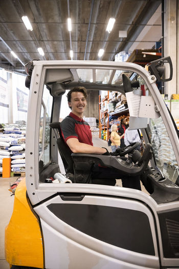 Side view of male warehouse worker sitting in forklift at warehouse
