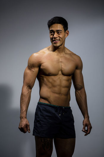 Shirtless muscular man standing against gray background