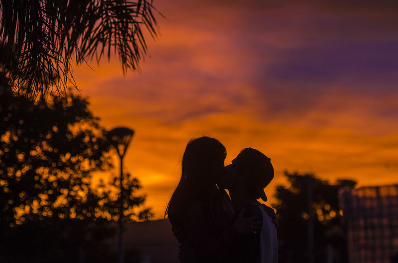 Side view of couple kissing against sky at sunset