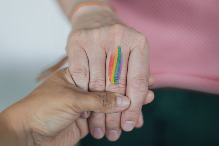 Two women interracial hands holding with the rainbow flag painted lgbtq