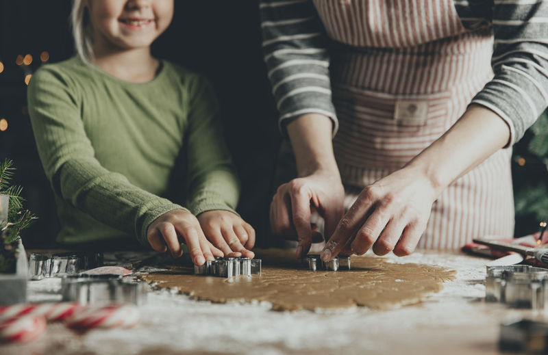 Mom and daughter or sisters make ginger bread cookies, cut shapes of cookies using mold at kitchen